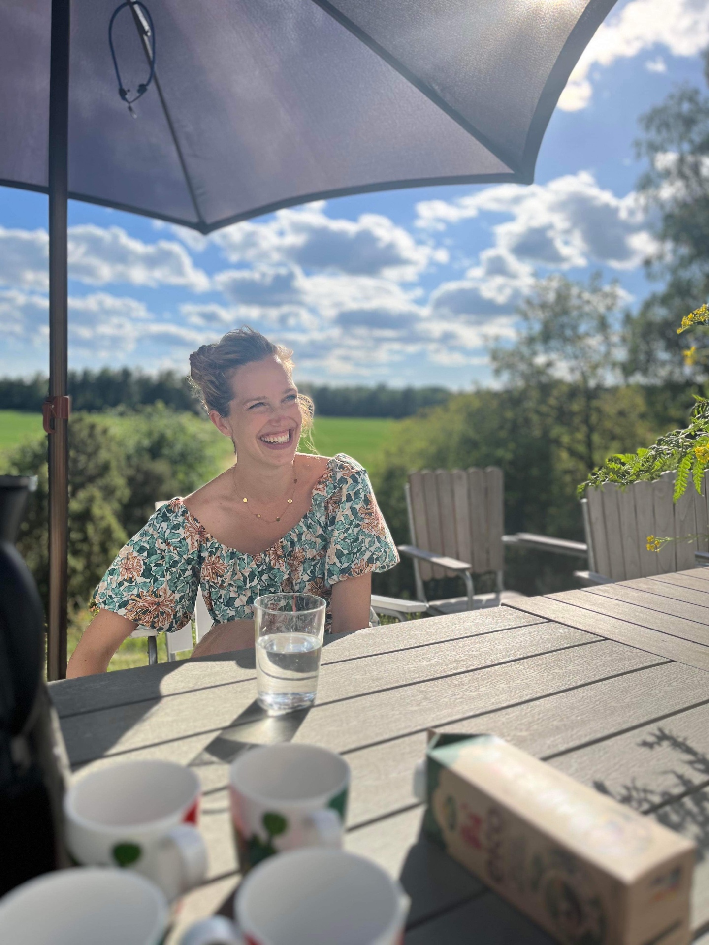 Linda skrattar vid ett bord i sommarsol